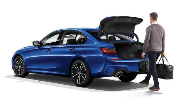 BMW 3-serie Sedan (G20), automatisk baklucka. Bild snett bakifrån av parkerad BMW 3-serie Sedan (G20) med förare som öppnar bakluckan automatiskt med foten.