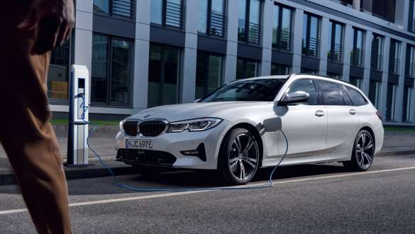 Laddhybrid BMW 3-serie Touring 2021 G21 sedd snett framifrån laddande Laddhybrid BMW 3-serie Touring 2021 G21 sedd snett framifrån laddande framför byggnad