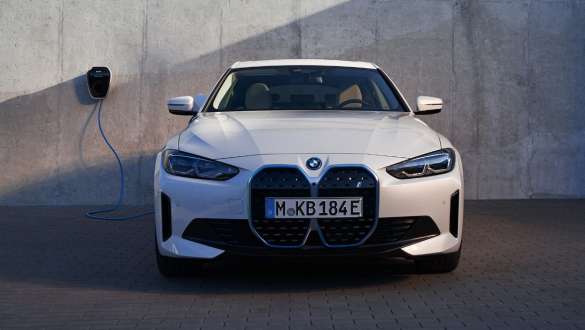 Sedd framifrån med BMW Wallbox BMW i4 eDrive40 G26 2021 BMW i4 eDrive40 G26 2021 Mineralvit sedd framifrån parkerad framför husvägg med BMW Wallbox laddningsstation