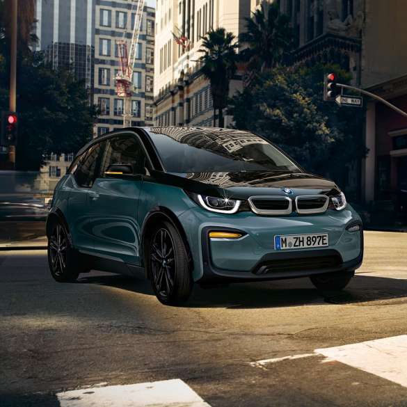 BMW i3 2018 sedd snett framifrån körandes BMW i3 I01 2018 Jucarobeige med accent Frozen Grey metallic sedd snett framifrån körandes i stadskuliss