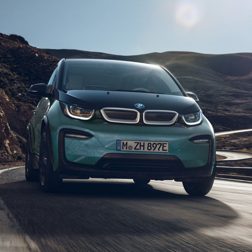 BMW i3 2018 sedd från sidan körandes BMW i3 I01 2018 Jucarobeige med accent Frozen Grey metallic sedd från sidan körandes framför stadskuliss