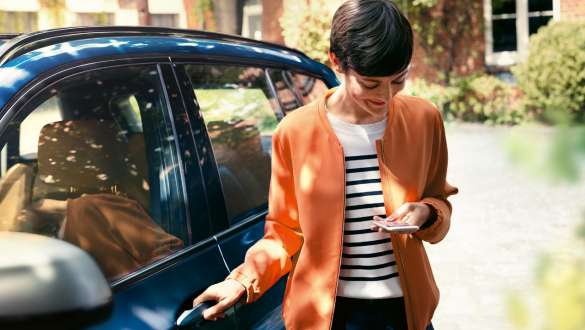 Kvinna kollar sin mobil och öppnar dörren till sin BMW BMW Teleservices kvinna kollar sin mobil och öppnar dörren till sin BMW
