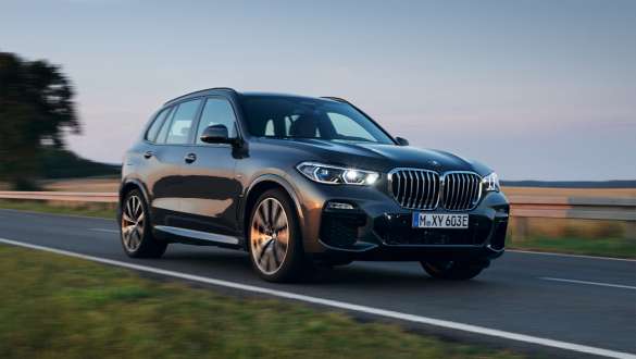 Plug-in hybrid BMW X5 xDrive45e sedd snett framifrån körandes Plug-in hybriden BMW X5 xDrive45e G05 sedd snett framifrån körandes på gatan