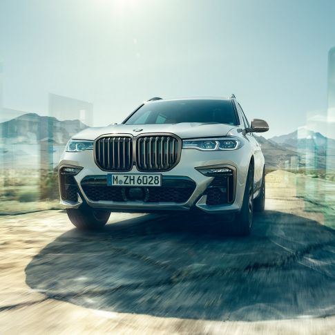 BMW X7 M50d, snett underifrån BMW X7 M50d: vit BMW X7 i rörelse sedd snett underifrån