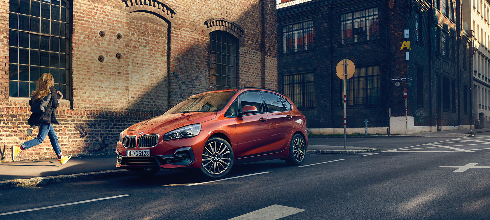 BMW 2-serie Active Tourer pågående parkering BMW 2-serie Active Tourer F45 Facelift 2018 Sunset Orange metallic sedd snett framifrån parkerad på gatan