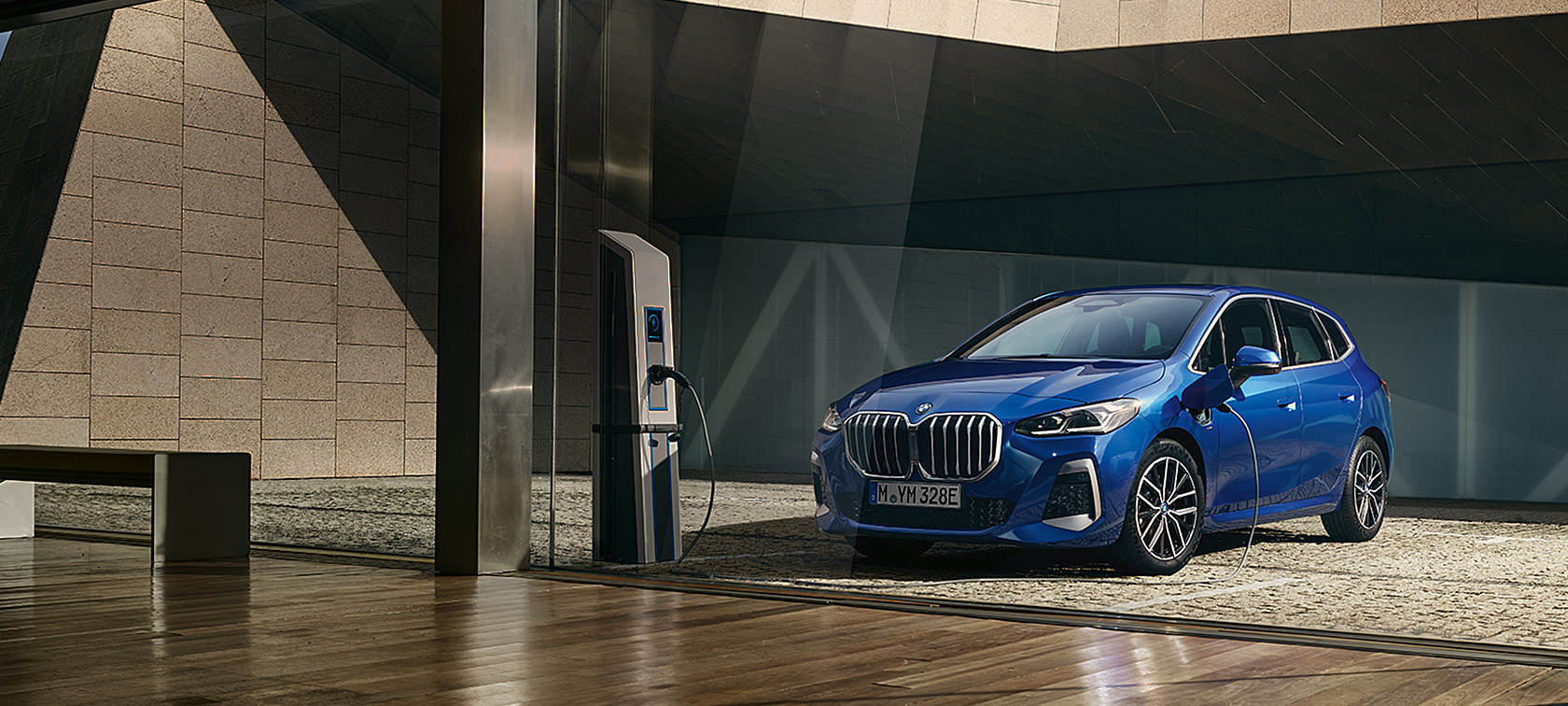 BMW 2-serie Active Tourer 230e laddhybrid U06 2021 Portimao Bl&aring; metallic sedd snett framifr&aring;n vid laddstolpen