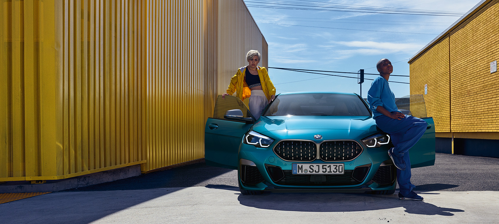 BMW 2-serie Gran Coupé F44, sedd framifrån BMW 2-serie Gran Coupé F44 Snapper Rocks Blå metallic med öppna dörrar och två personer vid bilen