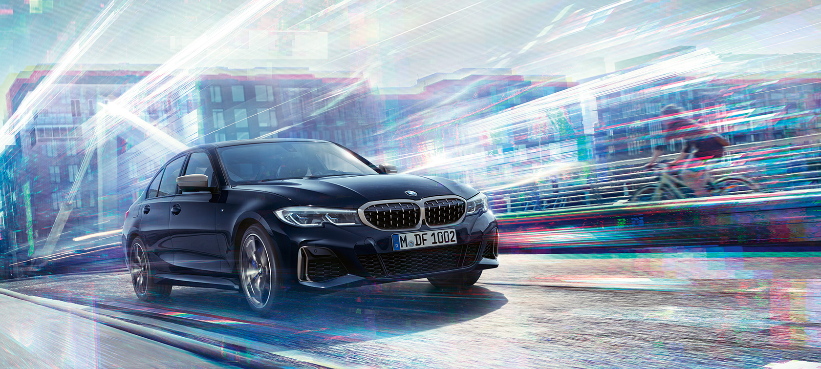 BMW 3-serie Sedan, BMW M340i xDrive. BMW M340i xDrive i rörelse snett från sidan på en väg med storstadsmiljö i bakgrunden.