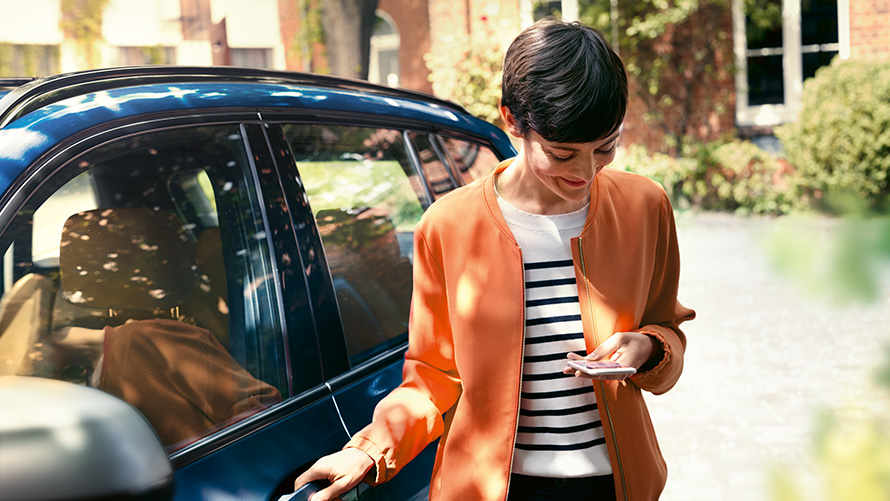 BMW Service Kvinna med smartphone i handen vid dörren till sin BMW BMW Service Kvinna med smartphone i handen vid dörren till sin BMW