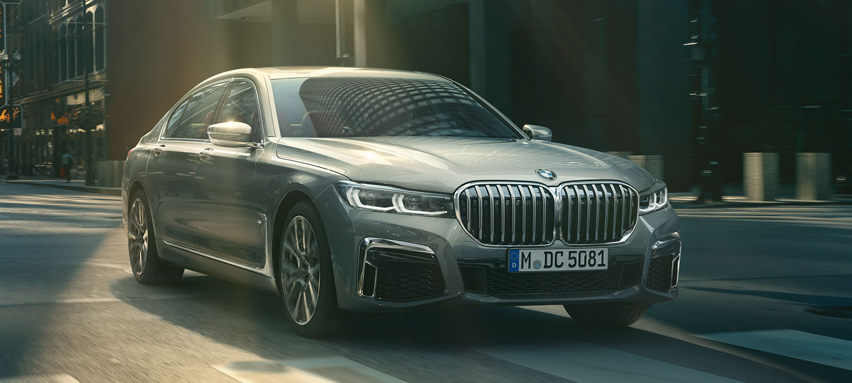 En grå BMW 7-serie sedan som kommer körande, trefjärdedels vy framifrån En grå BMW 7-serie sedan kör genom en stadsmiljö, trefjärdedels vy framifrån