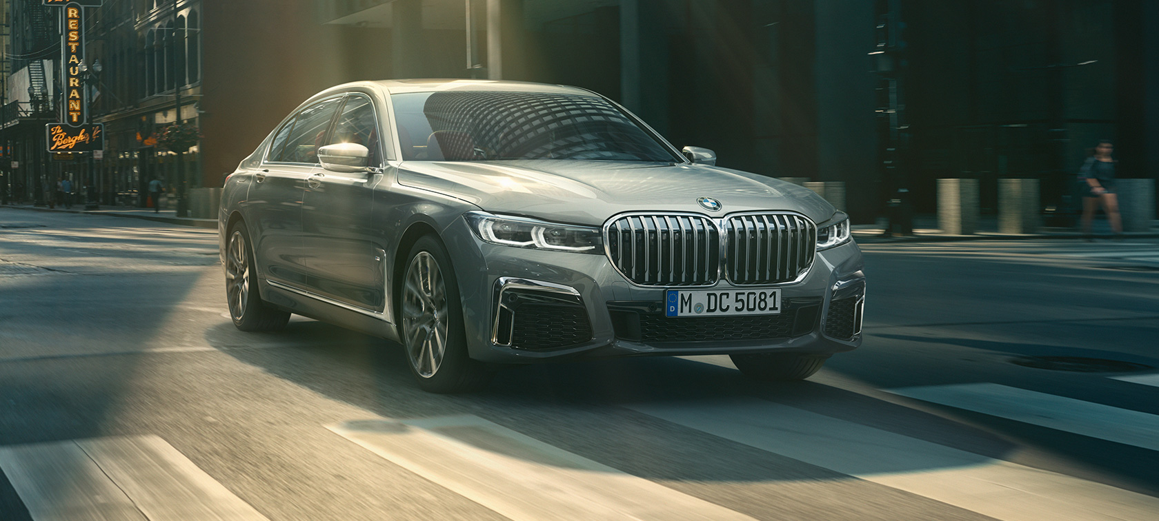 En grå BMW 7-serie Sedan kommer körande, sedd snett framifrån En grå BMW 7-serie Sedan kör genom en stadsmiljö, sedd snett framifrån