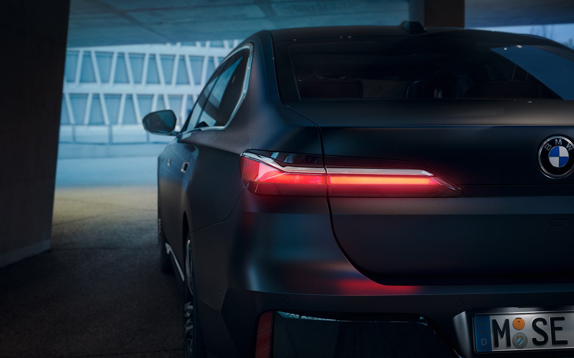 Sedd bakifrån BMW 7-serie Sedan G70 ICE 740i M sportpaket M Frozen Deep Grey metallic BMW 7-serie Sedan G70 ICE 740i M sportpaket M Frozen Deep Grey metallic sedd bakifrån med rödlysande bakljus i tunnel