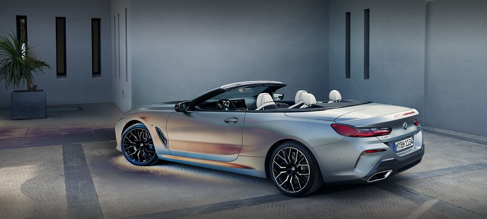 Man som lutar sig mot BMW 8-serie Cabriolet G14 LCI modellomarbetning 2022 BMW Individual Frozen Pure Grey metallic sidvy stående framför en byggnad