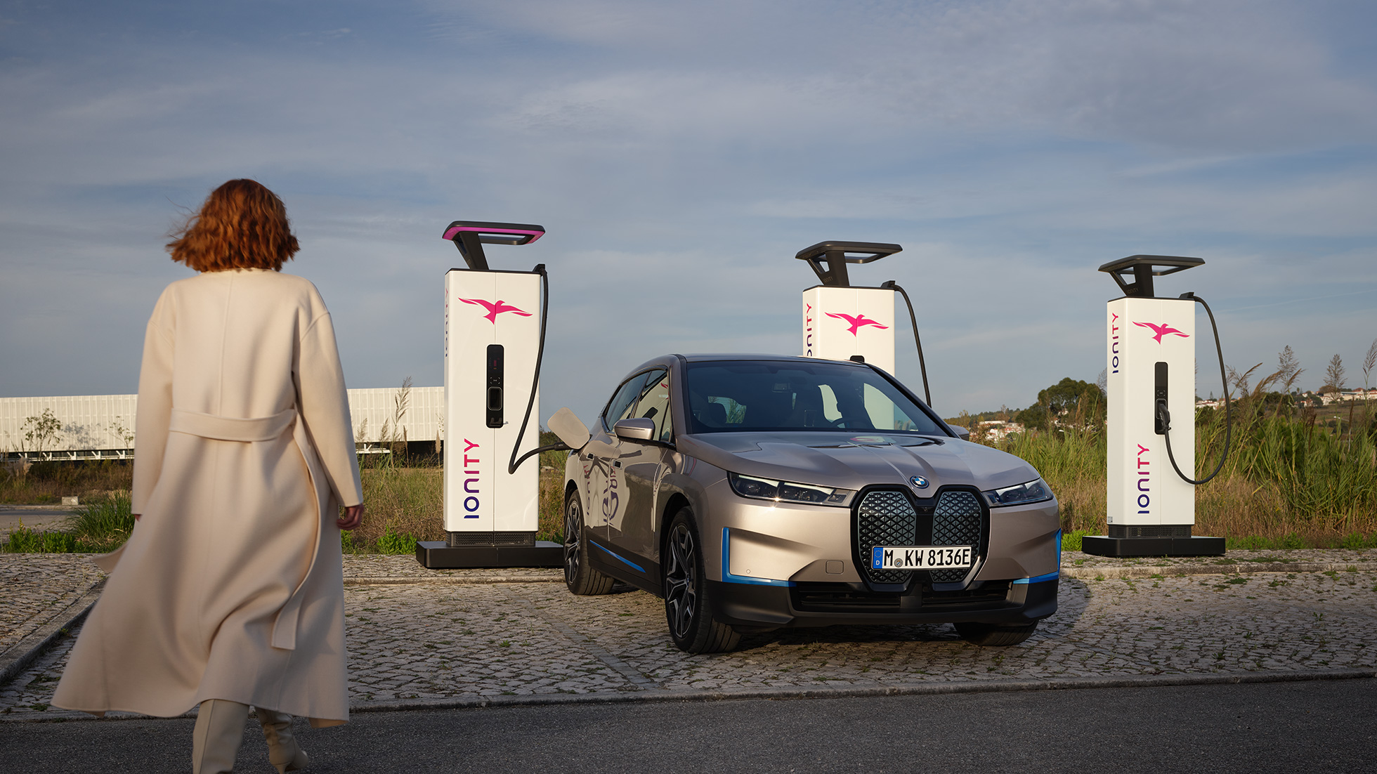 BMW iX sedd snett framifrån vid laddningsstation BMW iX Kashmirsilver i20 sedd snett framifrån vid laddningsstation