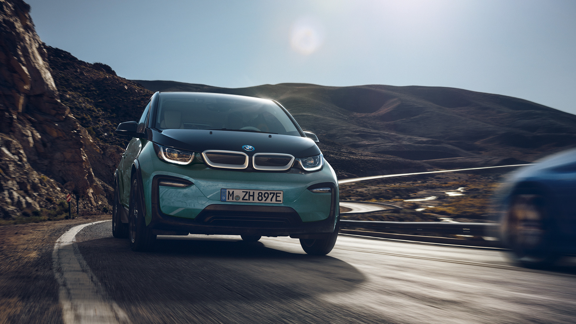 BMW i3 2018 sedd från sidan körandes BMW i3 I01 2018 Jucarobeige med accent Frozen Grey metallic sedd från sidan körandes framför stadskuliss