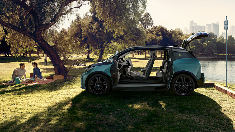 BMW i3 2018 i park BMW i3 I01 2018 Jucarobeige med accent Frozen Grey metallic sedd från sidan med öppna dörrar i park