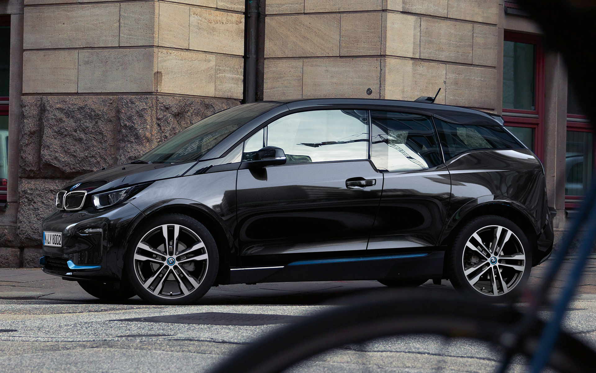 BMW i3s I01 2018 Fluid Black med accent BMW i Blå sidvy i stadskuliss körande