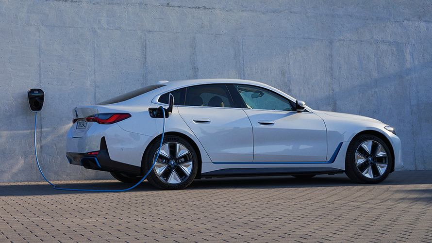 Sidovy av BMW Wallbox BMW i4 eDrive40 G26 2021 BMW i4 eDrive40 G26 2021 Mineralvit sedd från sidan parkerad framför husvägg med BMW Wallbox laddningsstation