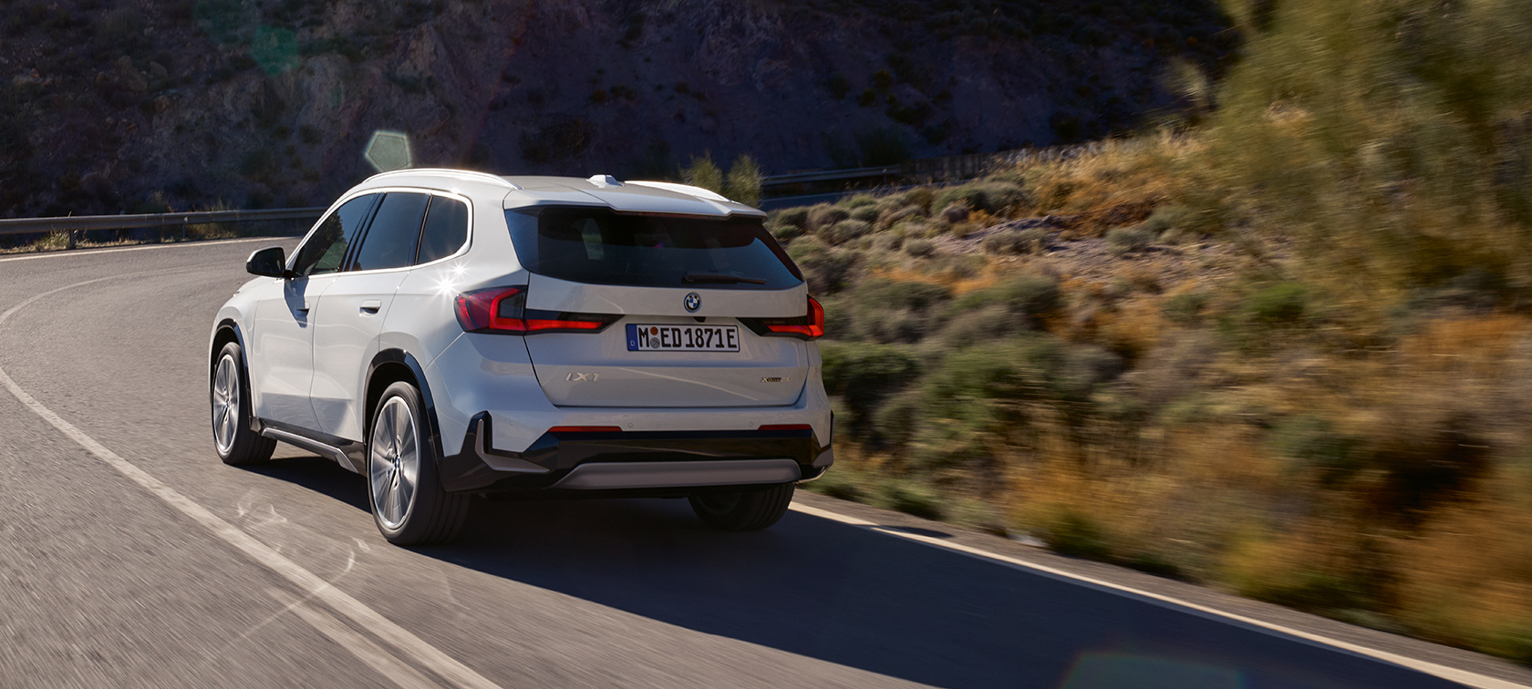 BMW iX1 U11 BEV kördynamik höjdpunkt video BMW iX1 U11 BEV 2022 Mineralvit metallic sedd körandes snett bakifrån på en bergsväg kördynamik höjdpunkt video