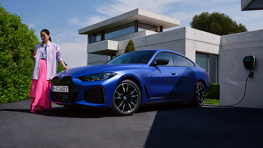 BMW i4 M50 G26 2021 BMW Individual Frozen Portimao Bl&aring; metallic sedd snett framifr&aring;n parkerad med kvinna framf&ouml;r hus