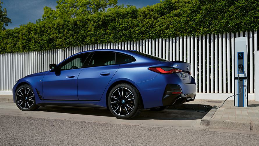 Sidovy BMW i4 M50 G26 2021 vid en publik snabbladdningsstation BMW i4 M50 G26 2021 BMW Individual Frozen Portimao Blå metallic sedd från sidan vid en publik snabbladdningsstation