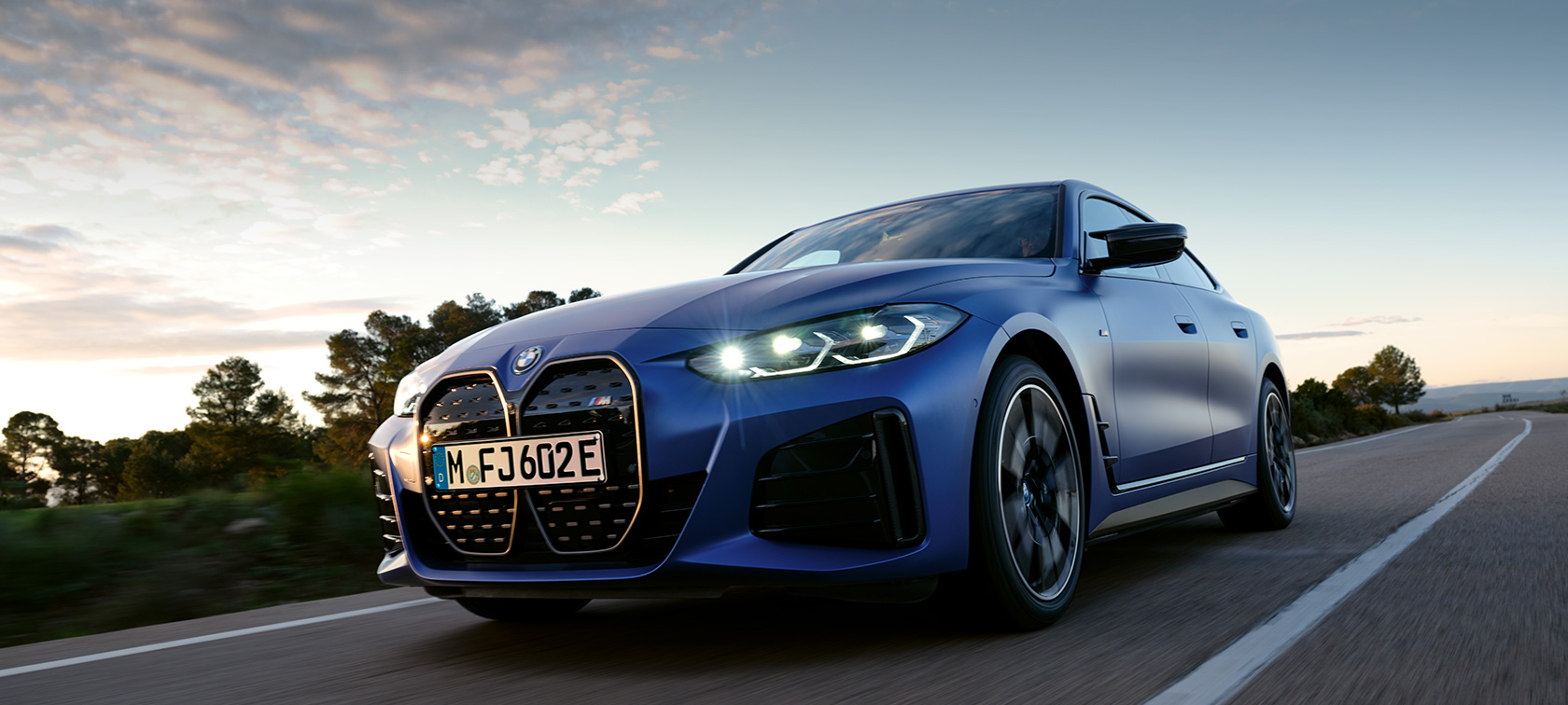 BMW i4 M50 G26 2021 sedd från sidan parkerad framför stenig terräng BMW i4 M50 2021 BMW Individual Frozen Portimao Blå metallic sedd snett från sidan parkerad framför stenig terräng