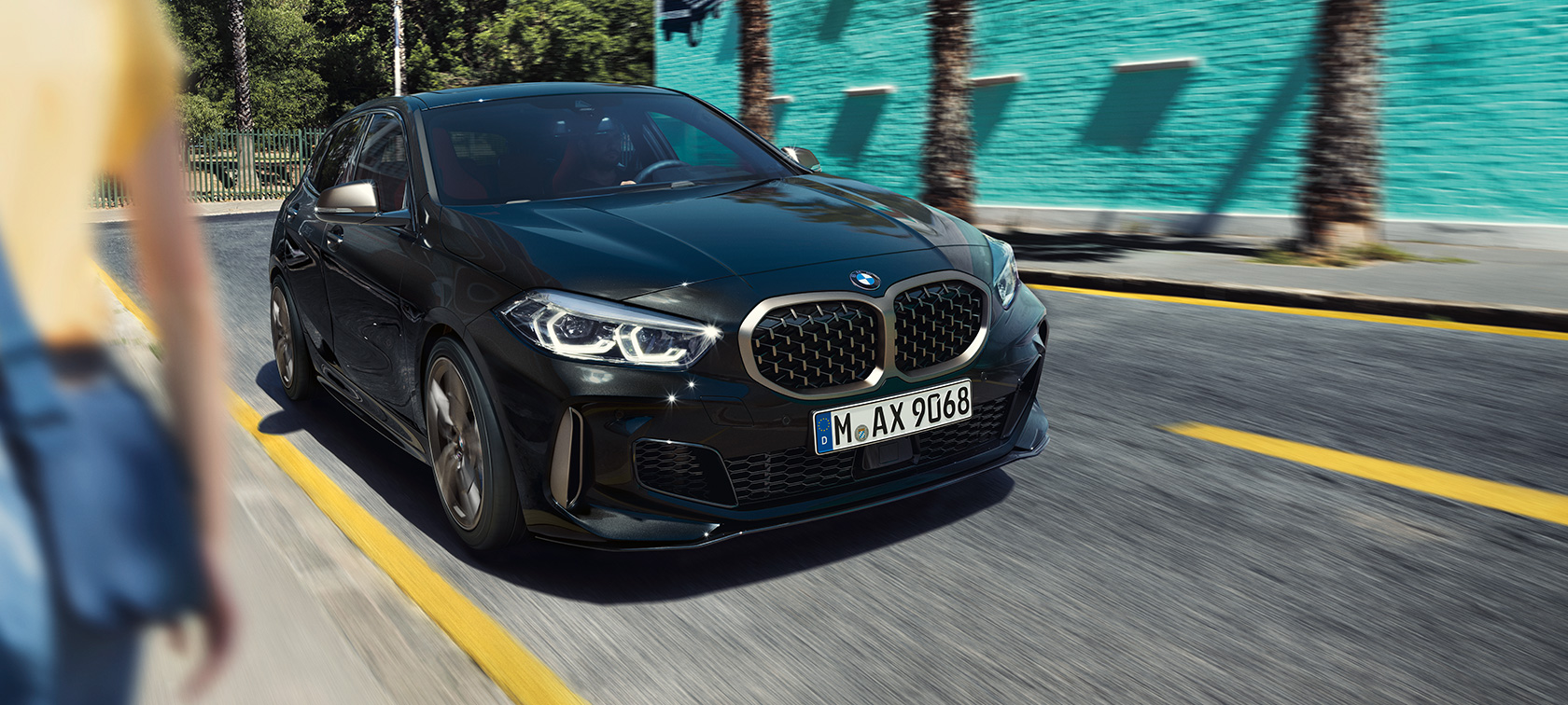 BMW M135i xDrive, trefjärdedelsvy framifrån. BMW M135i xDrive i safirsvart metallic, trefjärdelsvy framifrån, körande.