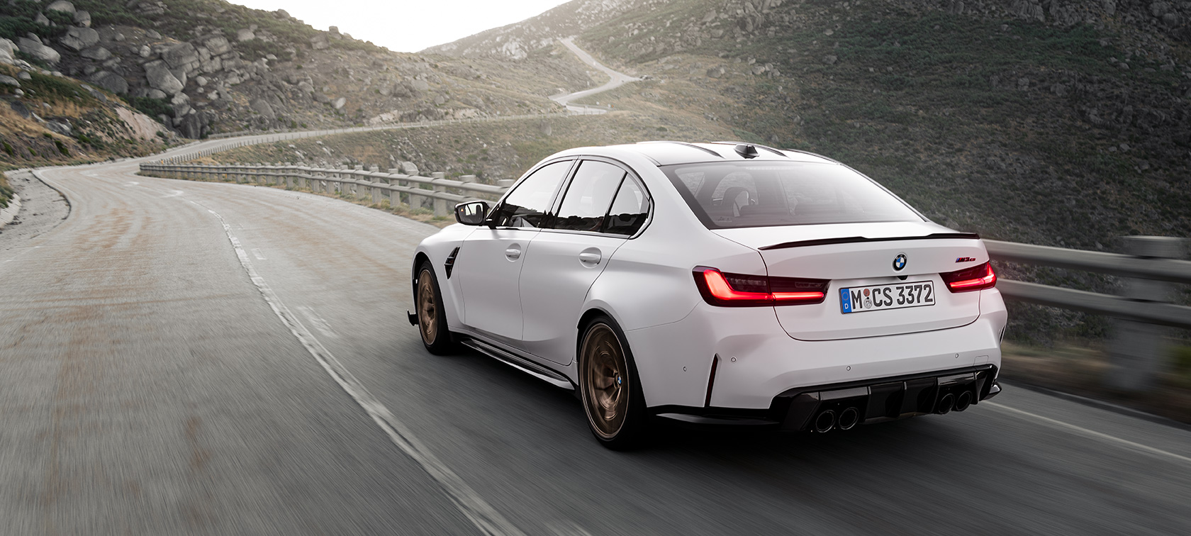 BMW M3 CS G80 sedd snett bakifrån körandes BMW M3 CS G80 sedd snett bakifrån körandes på vägen i bergen