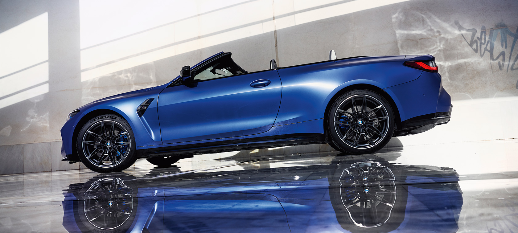 BMW M4 Competition Cabriolet med M xDrive G83 2021 sedd snett framifrån körande BMW M4 Competition Cabriolet med M xDrive G83 2021 BMW Individual Frozen Portimao Blå metallic sedd snett framifrån körande