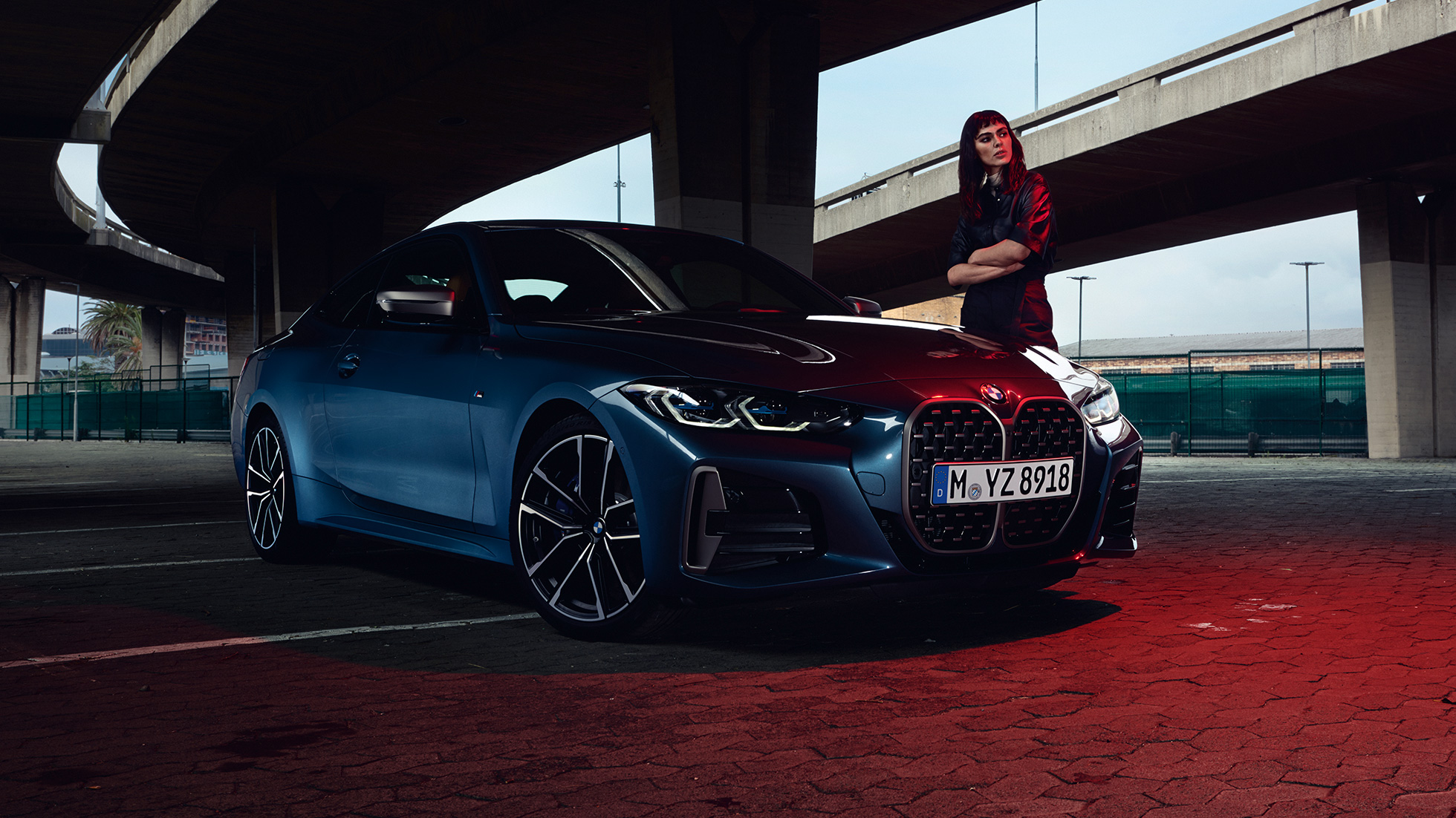 Modell står bredvid BMW M44i xDrive Coupé G22 2020, sedd snett från sidan BMW M440i xDrive Coupé Arctic Race Blue metallic G22 2020 sedd snett från sidan med modell