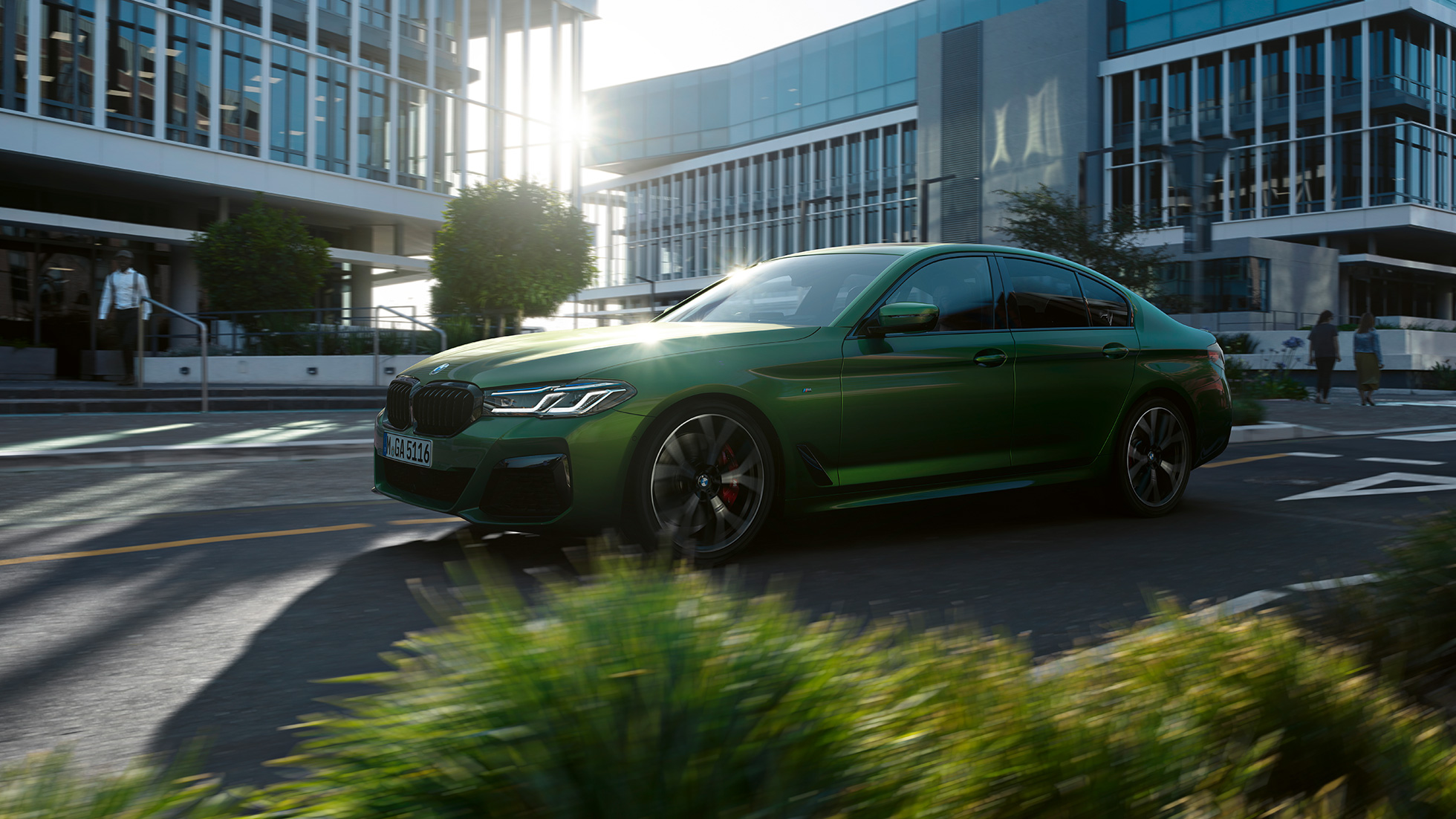 BMW M550i xDrive Sedan G30 LCI Facelift 2020 sedd i aktion från sidan BMW M550i xDrive Limousine G30 LCI Facelift 2020 BMW Individual Verde Ermes metallic sedd från sidan körandes i stan