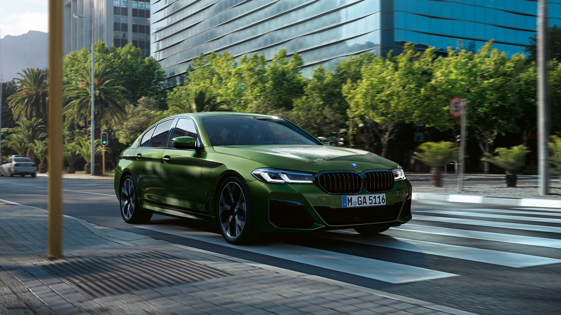 BMW M550i xDrive Sedan G30 LCI Facelift 2020 sedd i aktion snett framifrån BMW M550i xDrive Limousine G30 LCI Facelift 2020 BMW Individual Verde Ermes metallic sedd sett framifrån körandes i stan