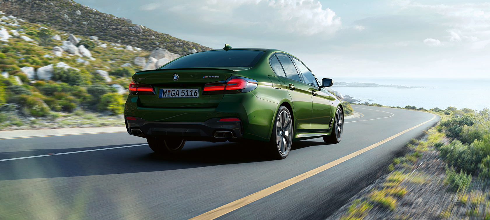BMW M550i xDrive Sedan G30 LCI Facelift 2020 sedd i aktion snett bakifrån BMW M550i xDrive Sedan G30 LCI Facelift 2020 BMW Individual Verde Ermes metallic sedd i aktion snett bakifrån