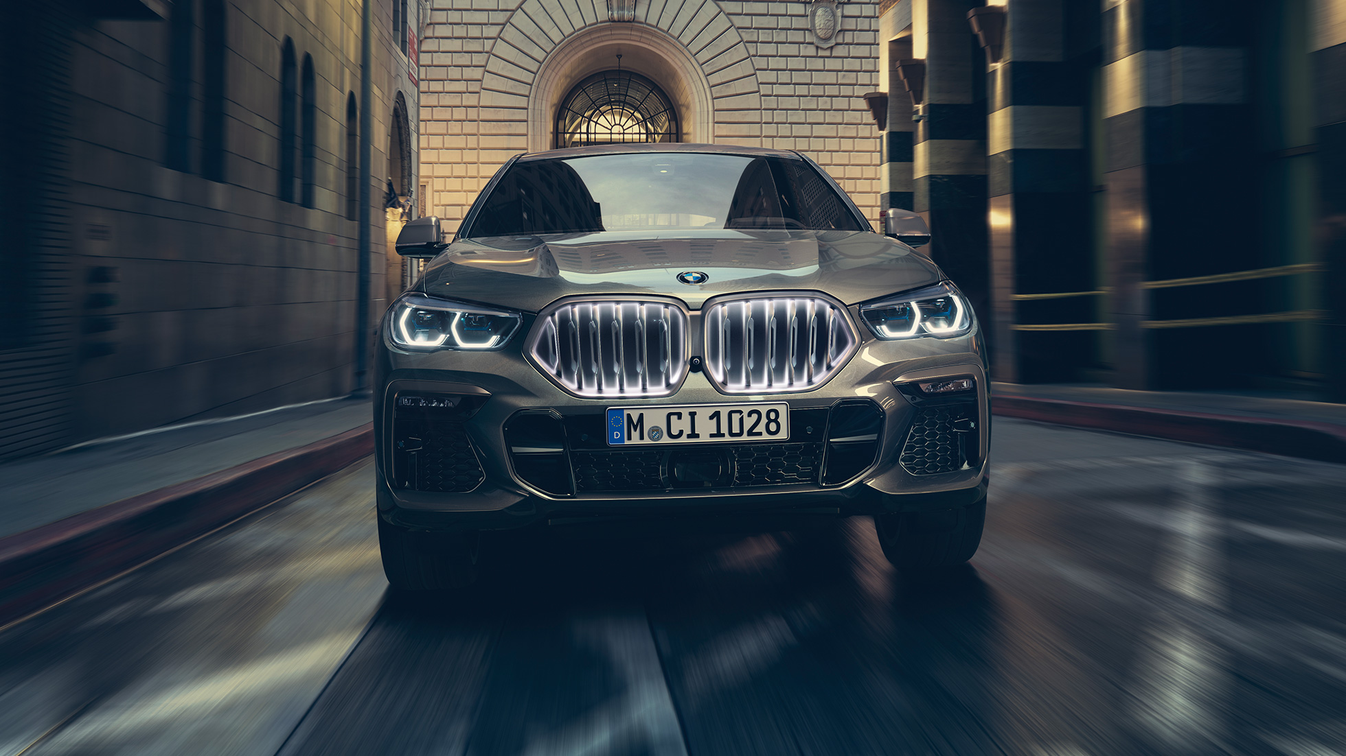 BMW X6 M50i med BMW-njure ‚Iconic Glow‘. BMW X6, sedd framifrån,parkerad framför stadsmiljö.