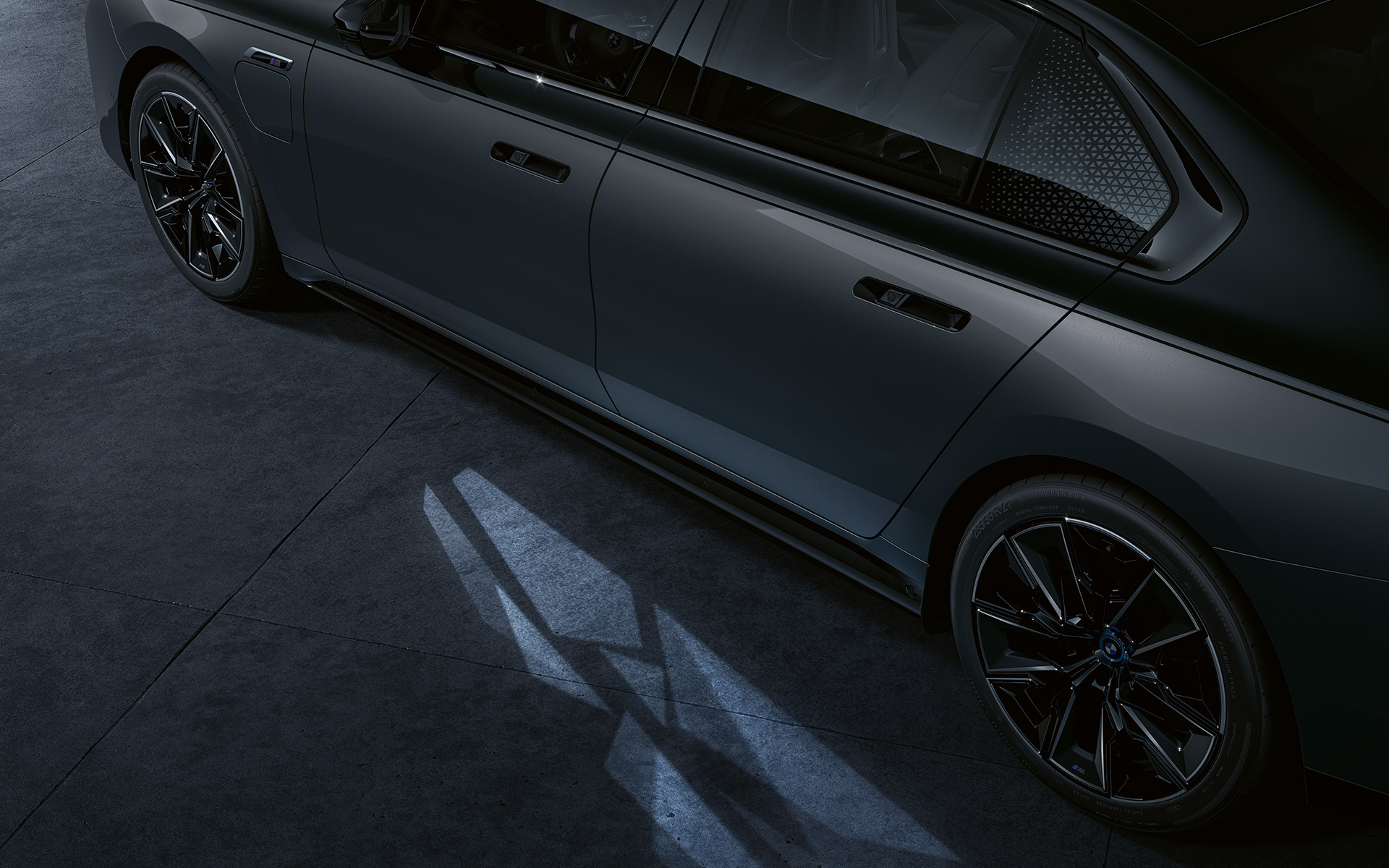 Ljuskoncept BMW M760e xDrive Sedan G70 BMW Individual tvåtonslack Safirsvart metallic BMW Individual Dravitgrå metallic närbild med tänd Welcome Light Carpet