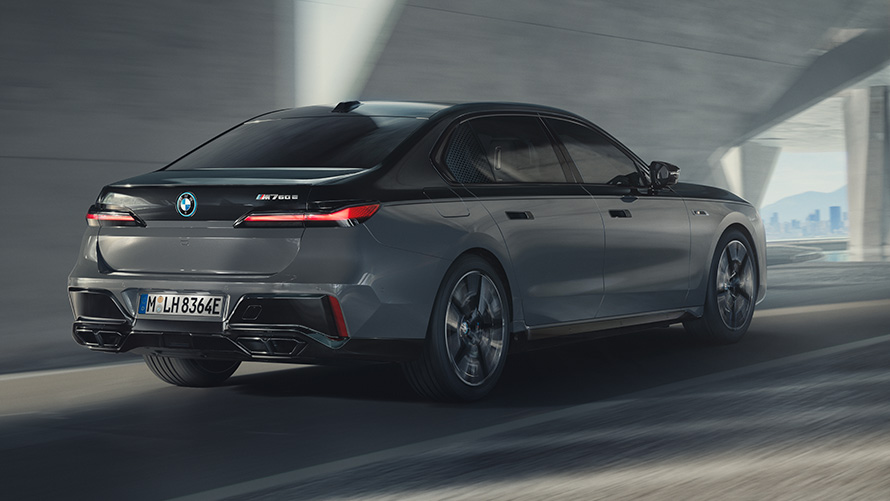 BMW M760e xDrive Sedan G70 M Performance-paket BMW M760e xDrive Sedan G70 M Performance-paket BMW Individual tvåtonslack Safirsvart metallic BMW Individual Dravitgrå metallic sedd snett bakifrån körande på väg