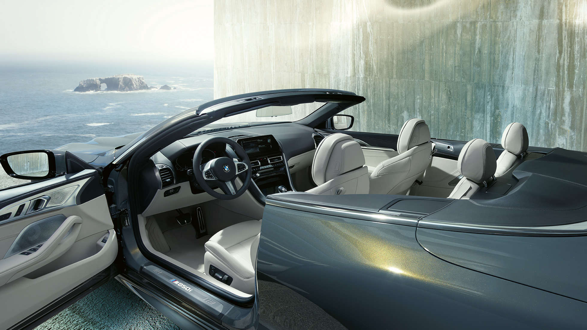 BMW M850i xDrive Cabriolet, interiör. BMW M850i xDrive Cabriolet i Dravitgrå metallic med öppnad sufflett, interiör med M läderratt och BMW Individual läderutrustning Merino Elfenbensvit.