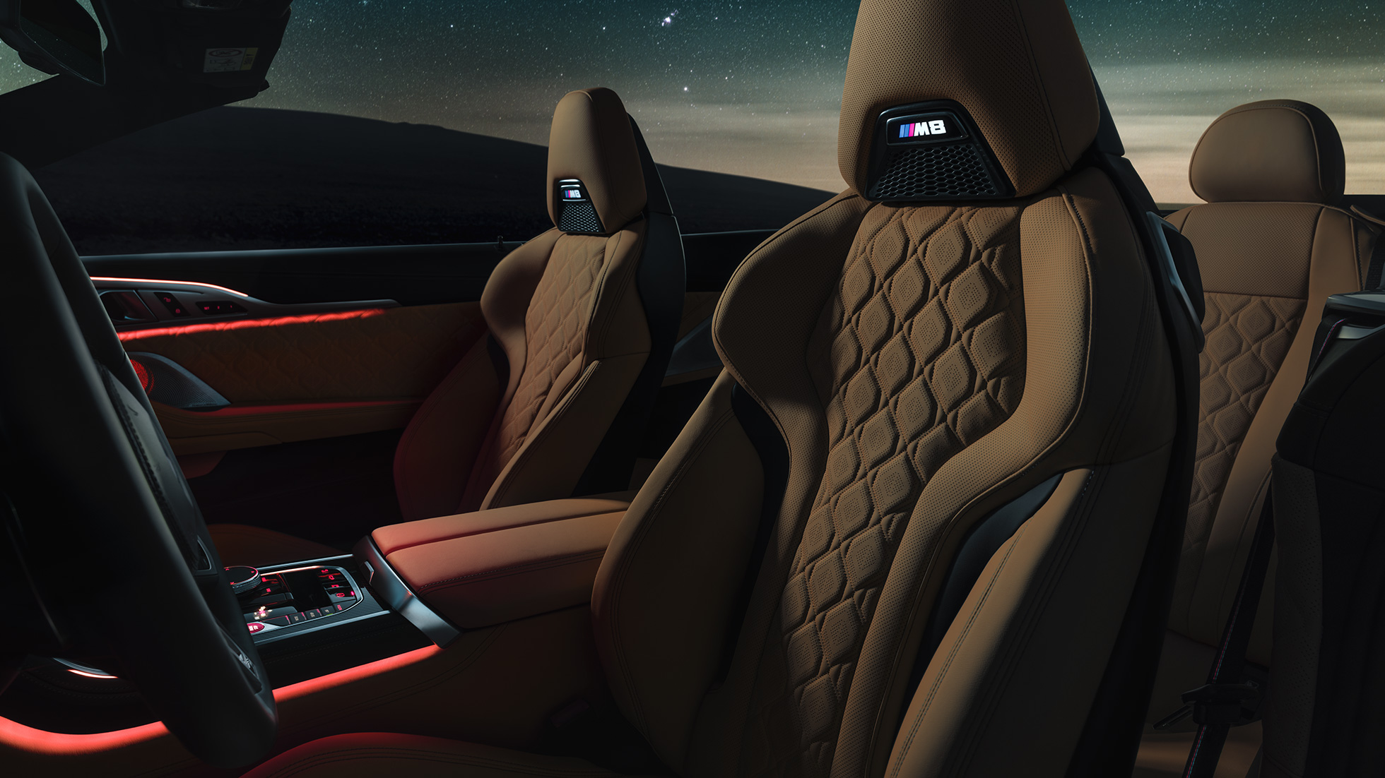 M sportstolar i läder Merino. BMW M8 Competition Cabriolet med öppnad sufflett under stjärnhimmel, kupé med M sportstolar i läder Merino och röd stämningsbelysning.