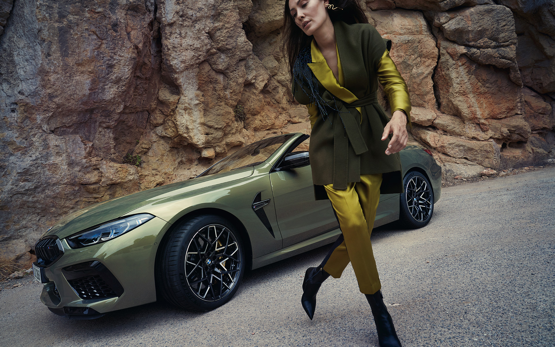 BMW M8 Competition Cabriolet F91 LCI 2022 sedd snett framifrån parkerad i stenig terräng BMW M8 Competition Cabriolet F91 LCI Facelift 2022 BMW Individual Brass metallic sedd snett framifrån parkerad i stenig terräng med kvinnlig modell