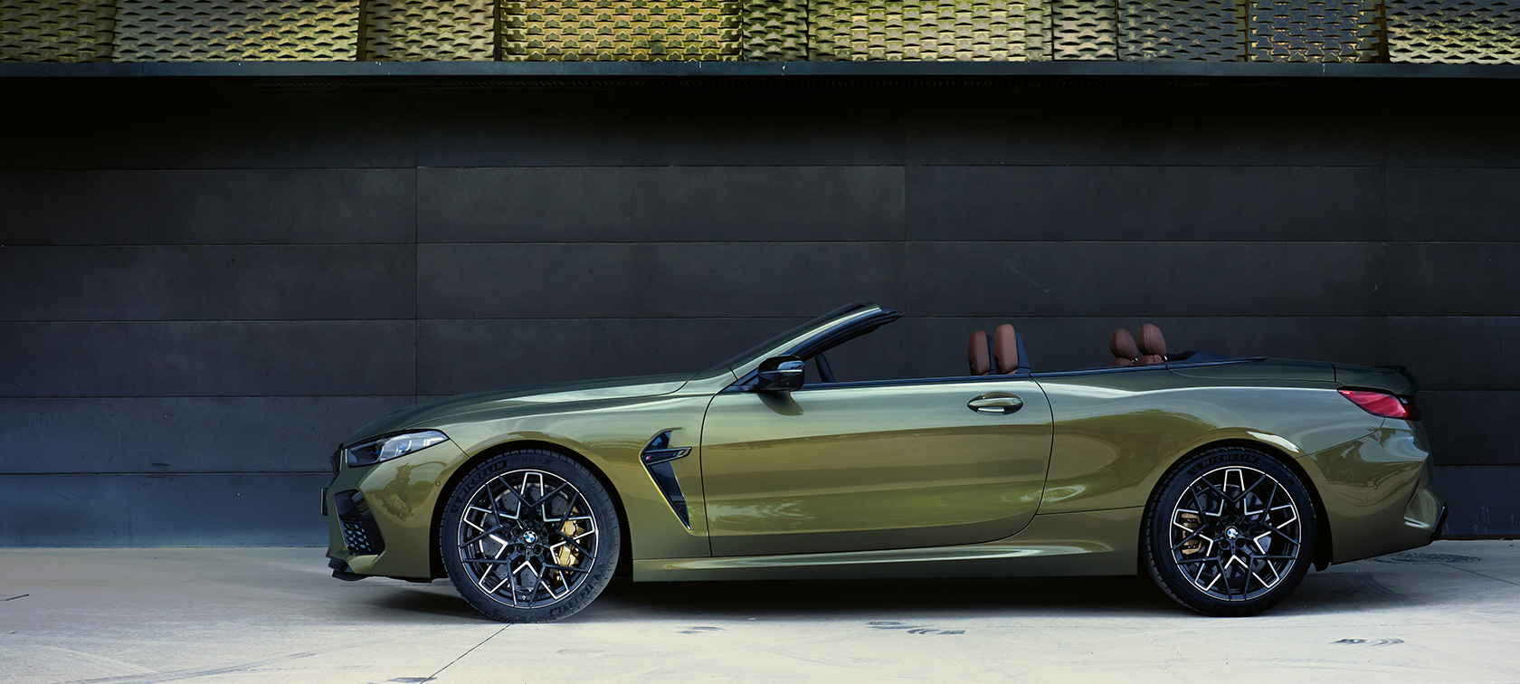 BMW M8 Competition Cabriolet F91 LCI Facelift 2022 sidvy parkerad BMW M8 Competition Cabriolet F91 LCI Facelift 2022 BMW Individual Brass metallic sedd från sidan parkerad med öppen dörr och kvinnlig modell