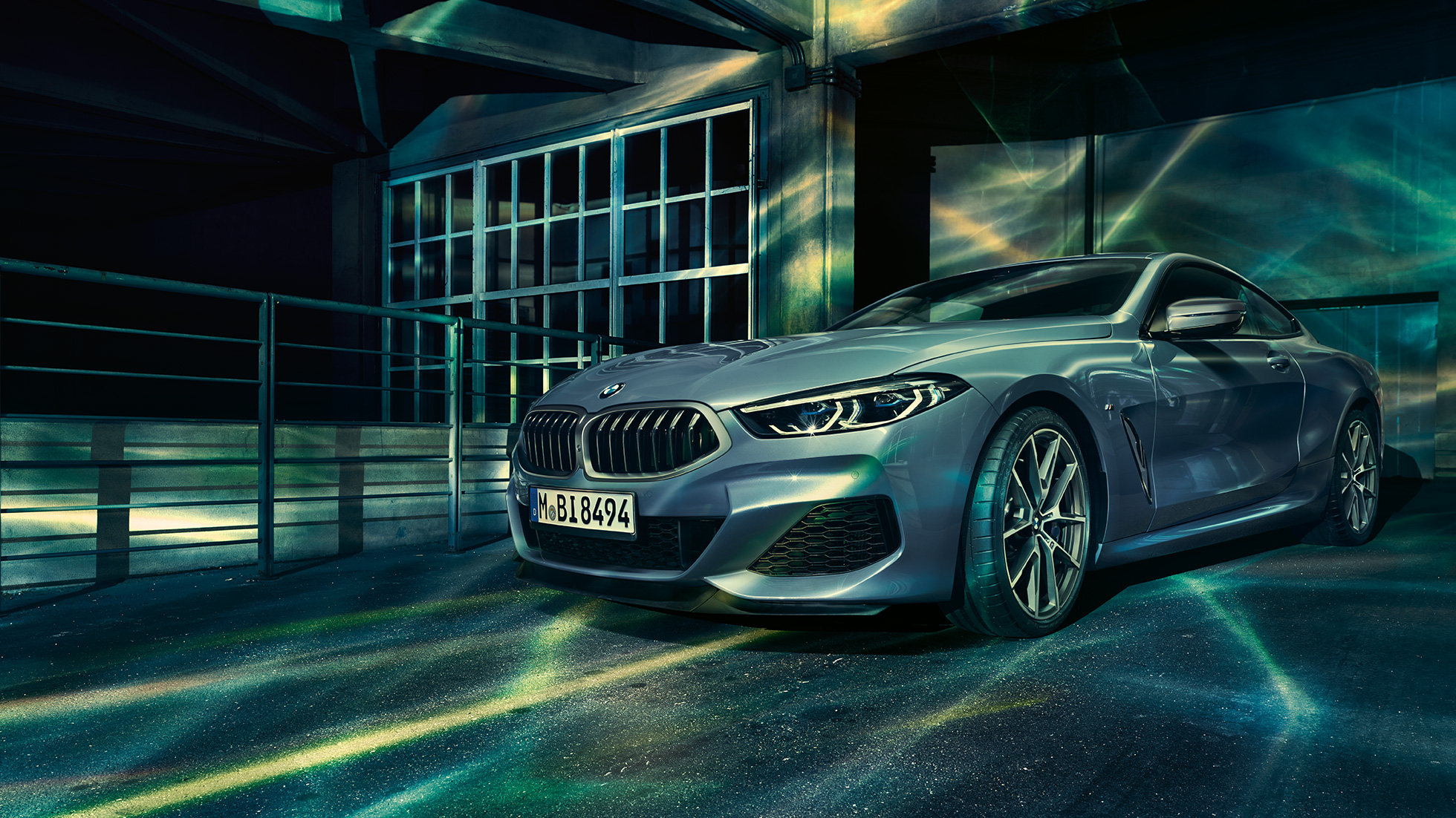 BMW M850i xDrive Coupé, trefjärdedelsvy framifrån. BMW M850i xDrive Coupé i Barcelona Blåmetallic, trefjärdedelsvy framifrån, parkerad framför byggnad.