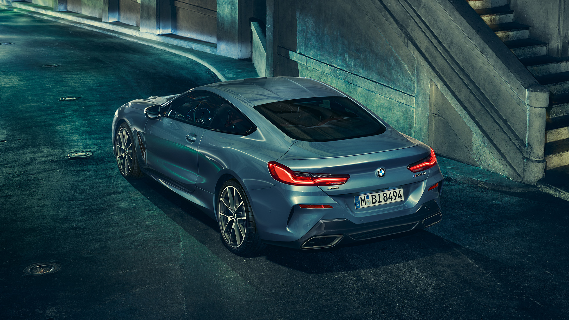 BMW M850i xDrive Coupé, trefjärdedelsvy bakifrån från vänster. BMW M850i xDrive Coupé i Barcelona Blåmetallic, trefjärdedelsvy snett bakifrån från vänster, körning på natten.