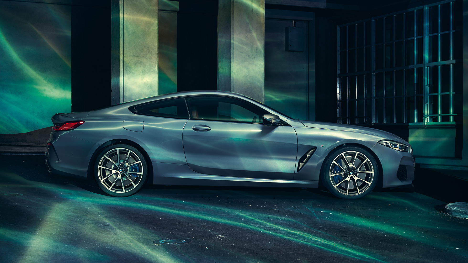 BMW M850i xDrive Coupé, sedd från sidan. BMW M850i xDrive Coupé i Barcelona Blåmetallic, sedd från sidan, parkerad framför byggnad.