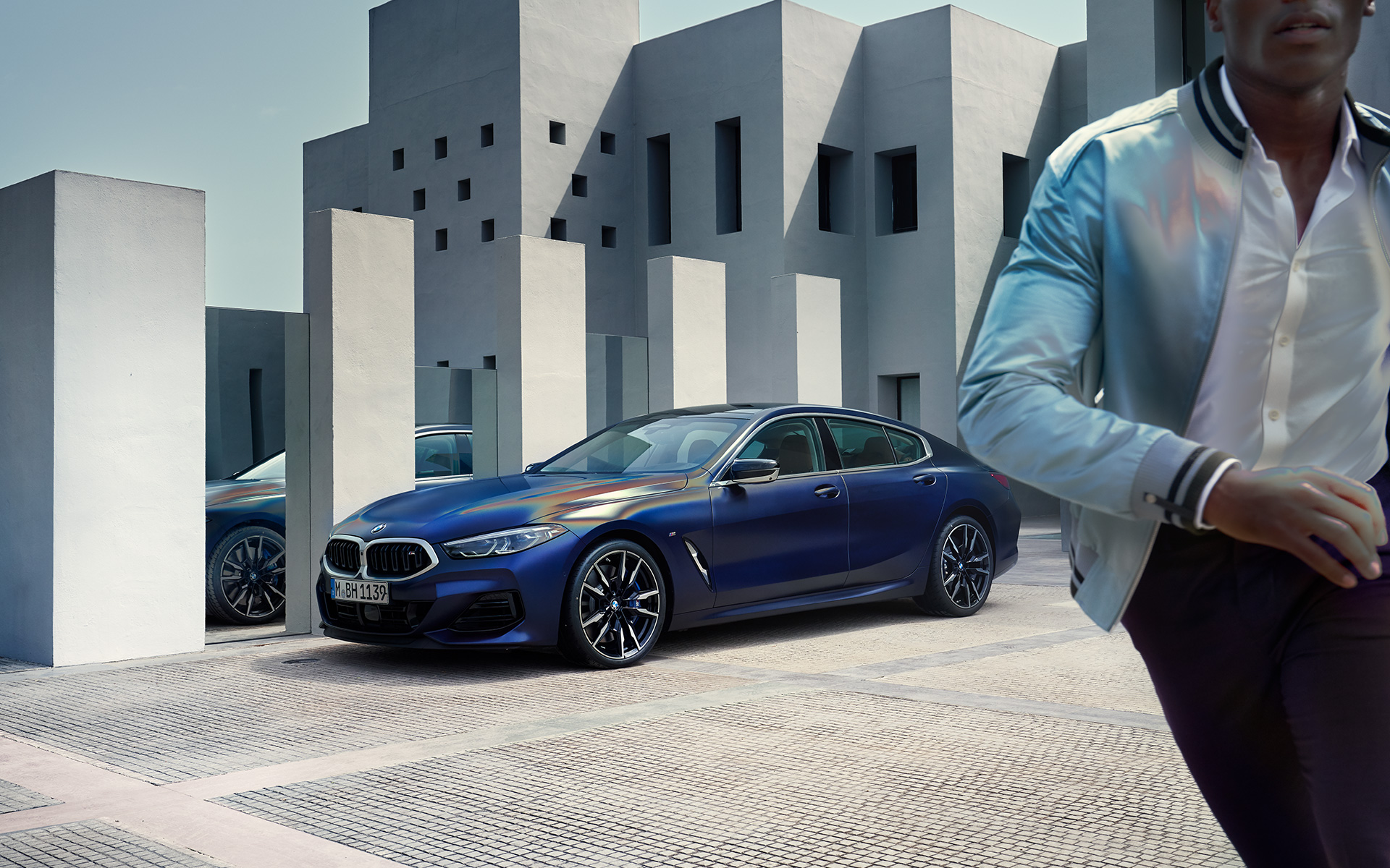 Snett framifrån BMW M850i xDrive Gran Coupé G16 LCI Facelift 2022 BMW M850i xDrive Gran Coupé G16 LCI Facelift 2022 BMW Individual Frozen Tansanitblå metallic sedd snett framifrån stående med manlig modell i förgrunden