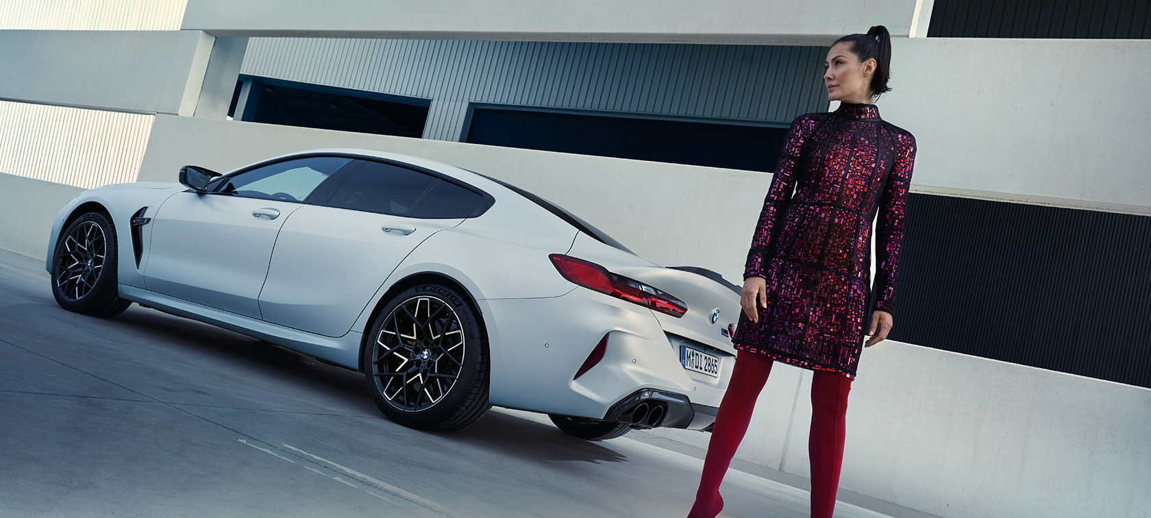 Snett bakifrån BMW M8 Competition Gran Coupé F93 LCI 2022 BMW M8 Competition Gran Coupé F93 LCI Facelift 2022 BMW Individual Frozen Brilliant White metallic sedd snett bakifrån med kvinnlig modell bredvid bilen