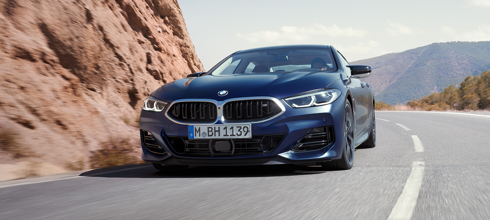 Snett framifrån körandes BMW M850i xDrive Gran Coupé G16 LCI Facelift 2022 BMW M850i xDrive Gran Coupé G16 LCI Facelift 2022 BMW Individual Frozen Tansanitblå metallic sedd snett framifrån körandes i en kurva
