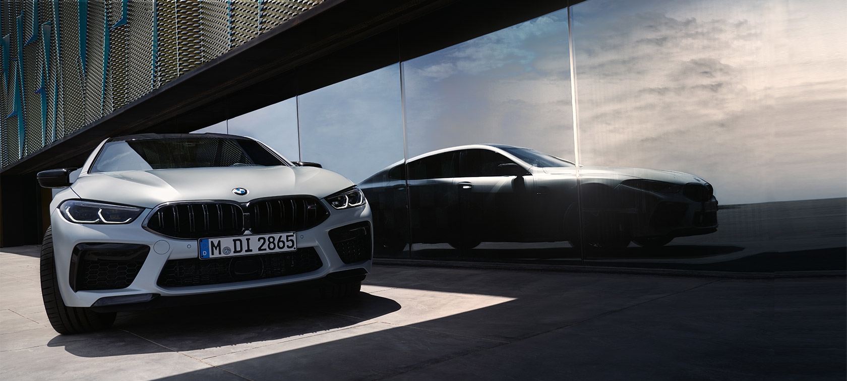 Frontvy BMW M8 Competition Gran Coupé F93 LCI Facelift 2022 BMW M8 Competition Gran Coupé F93 LCI Facelift 2022 BMW Individual BMW Individual Frozen Brilliant White metallic sedd framifrån med reflekterad silhuett framme på rutan