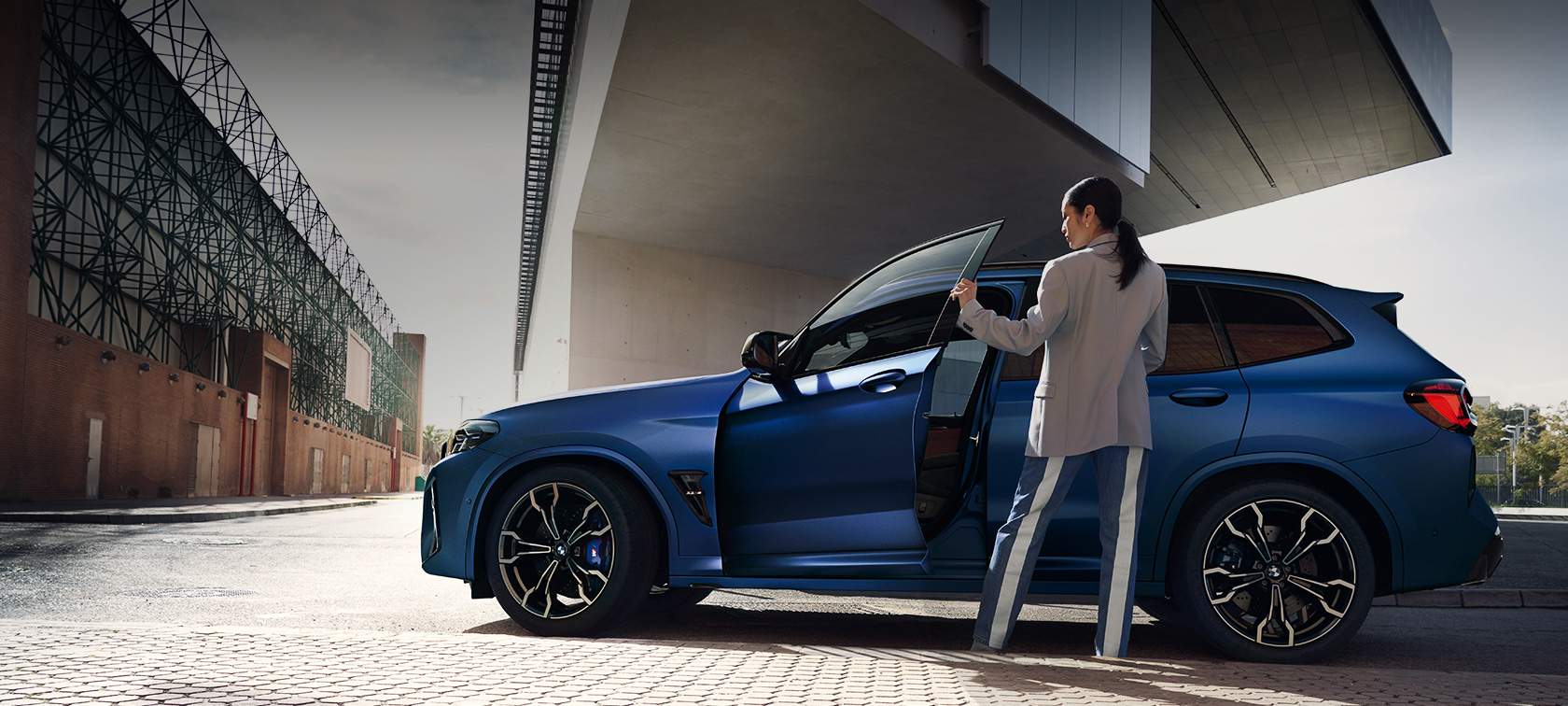 BMW X3 M Competition F97 LCI Facelift 2021 sedd från sidan parkerad BMW X3 Competition F97 LCI Facelift 2021 BMW Individual Frozen Portimao blåmetallic sedd från sidan parkerad med öppen dörr och kvinnlig modell