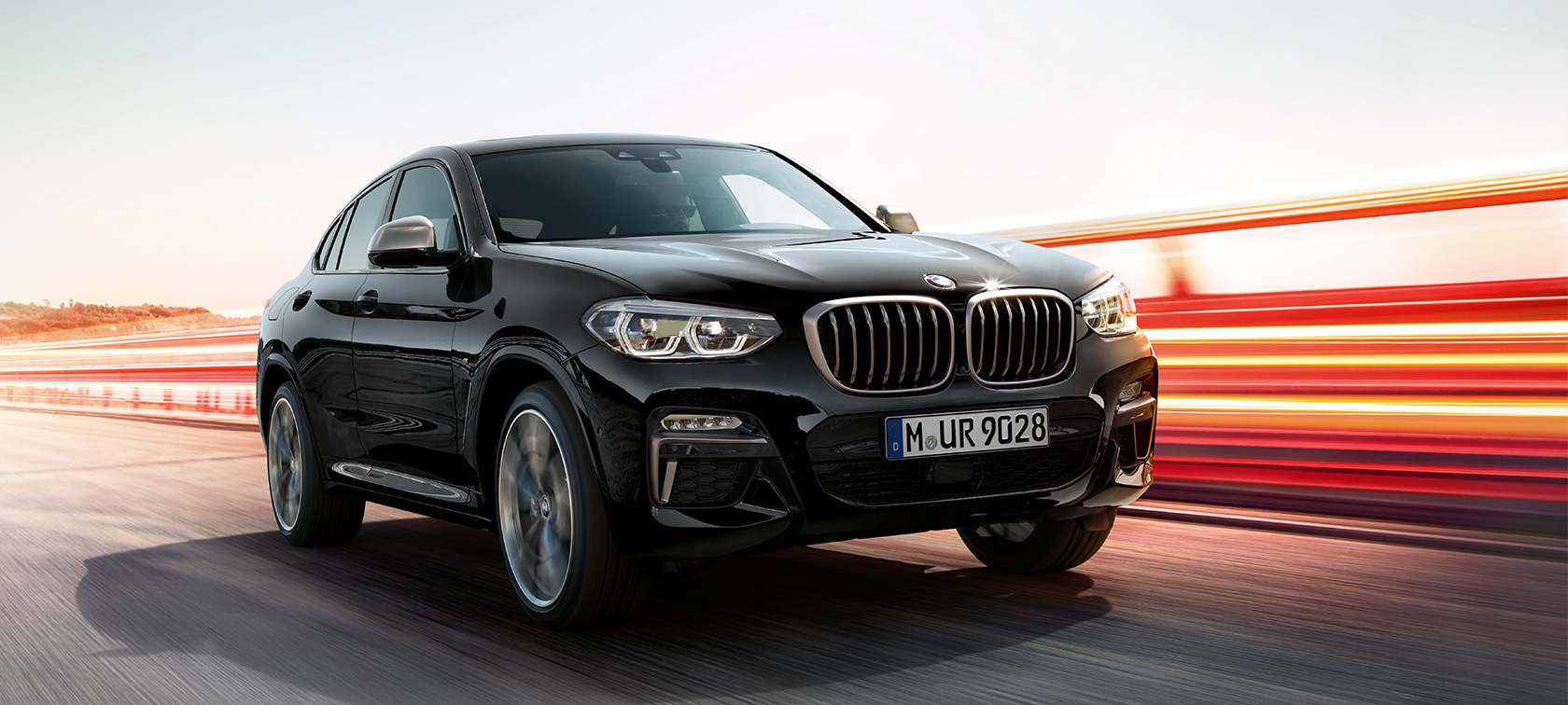 BMW X4 M40i och BMW X4 M40d, trefjärdedels vy framifrån från vänster. BMW X4 M40i och BMW X4 M40d i Safirsvart metallic, kommer körande, Exteriör, trefjärdedels vy framifrån från vänster med ljusstrimmor.