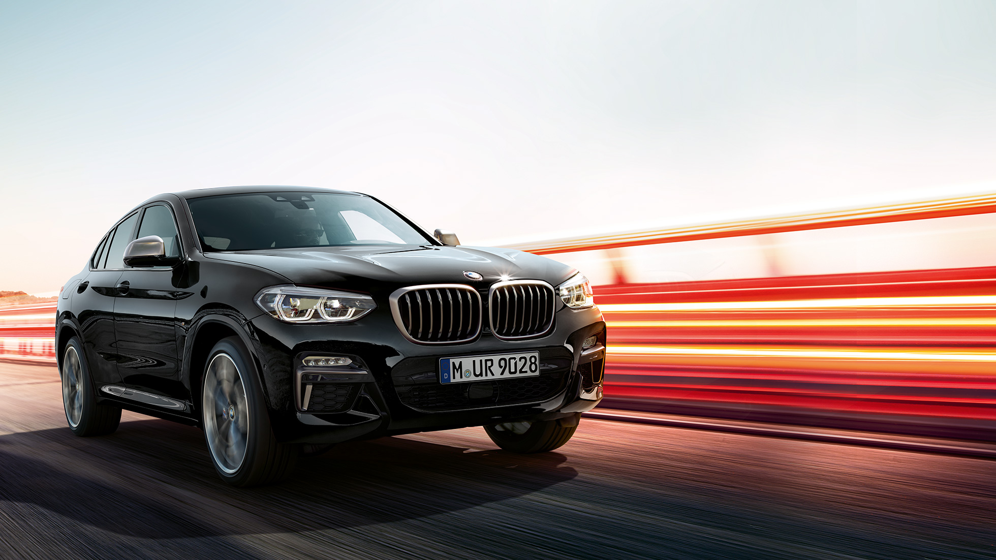BMW X4 M40i, Trefjärdedels vy bakifrån. BMW X4 M40i i Safirsvart metallic, kommer körande, Exteriör, trefjärdedels vy bakifrån med ljusstrimmor.